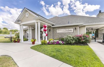 A building with the sign "Aventura of Mid River" is surrounded by a well-kept lawn and flower beds.